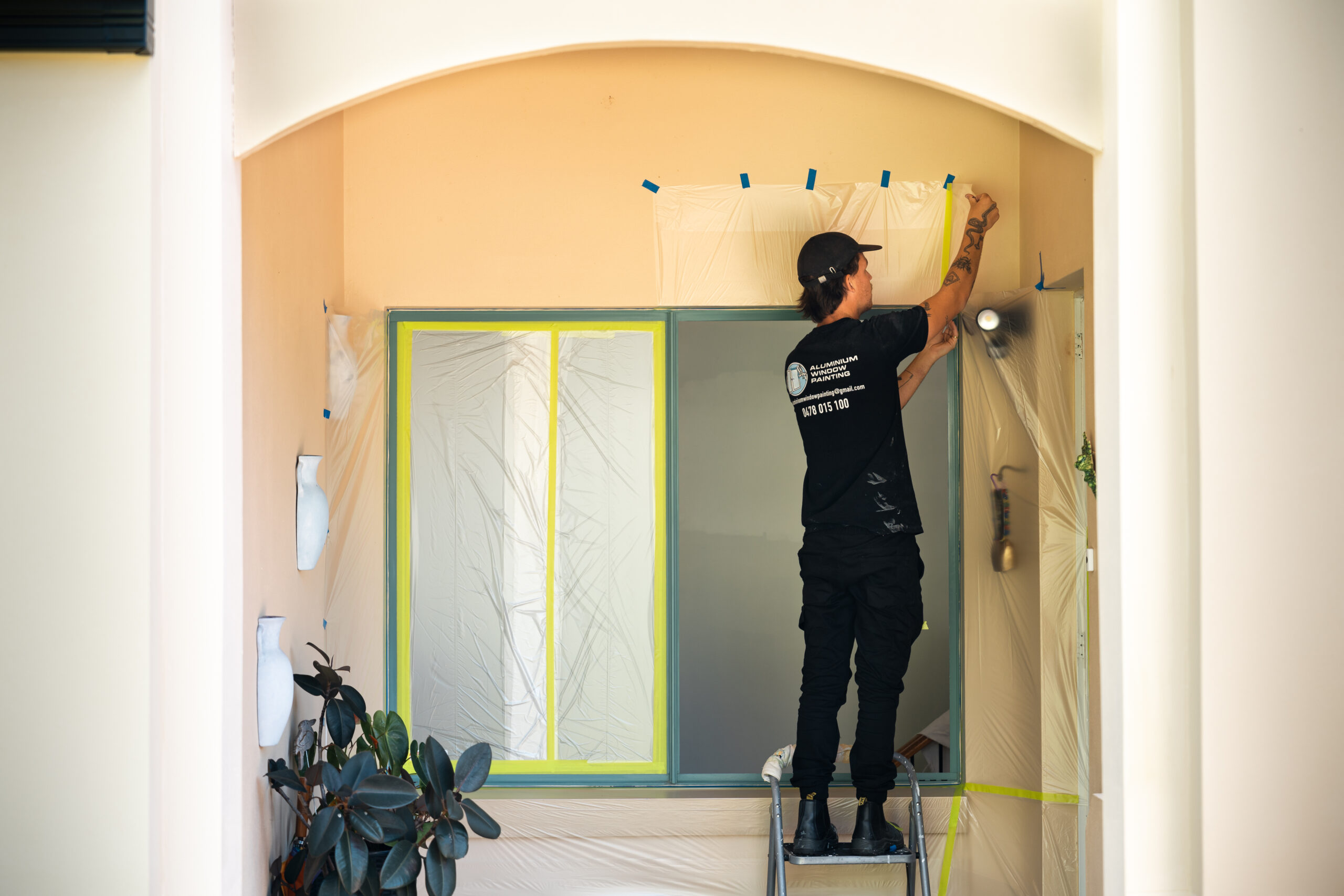 Ben from Aluminium Window Painting is masking up an old green window frame to be resprayed.
